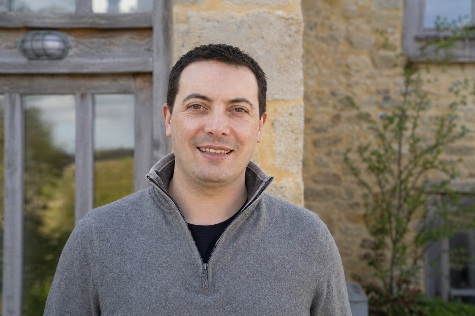 Portrait of Iain from the Wottz team smiling in a navy jacket outside a Cotswolds stone building