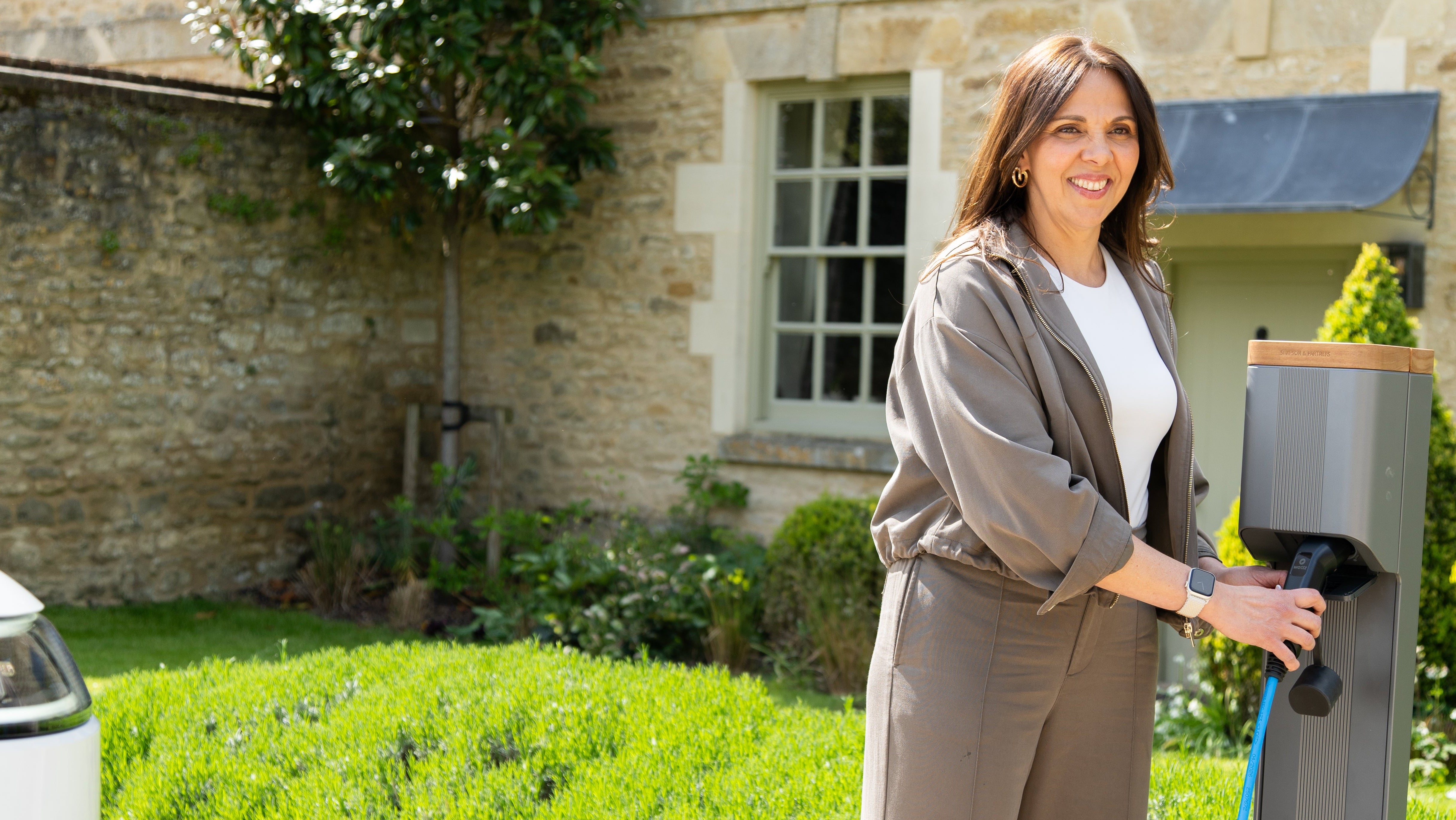Woman connecting a blue Wottz cable to a Simpson & Partners charge post at a Cotswolds house