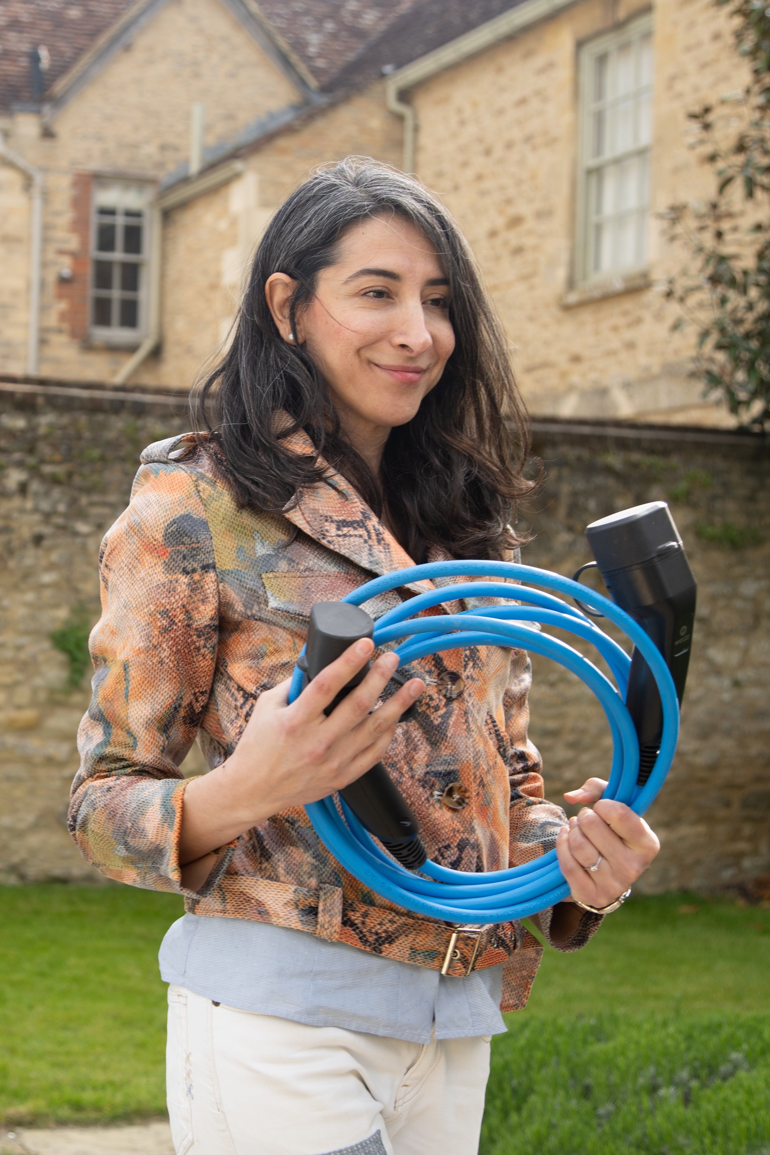 Woman holding a coiled blue Wottz Type 2 charging cable outside a Cotswolds stone cottage