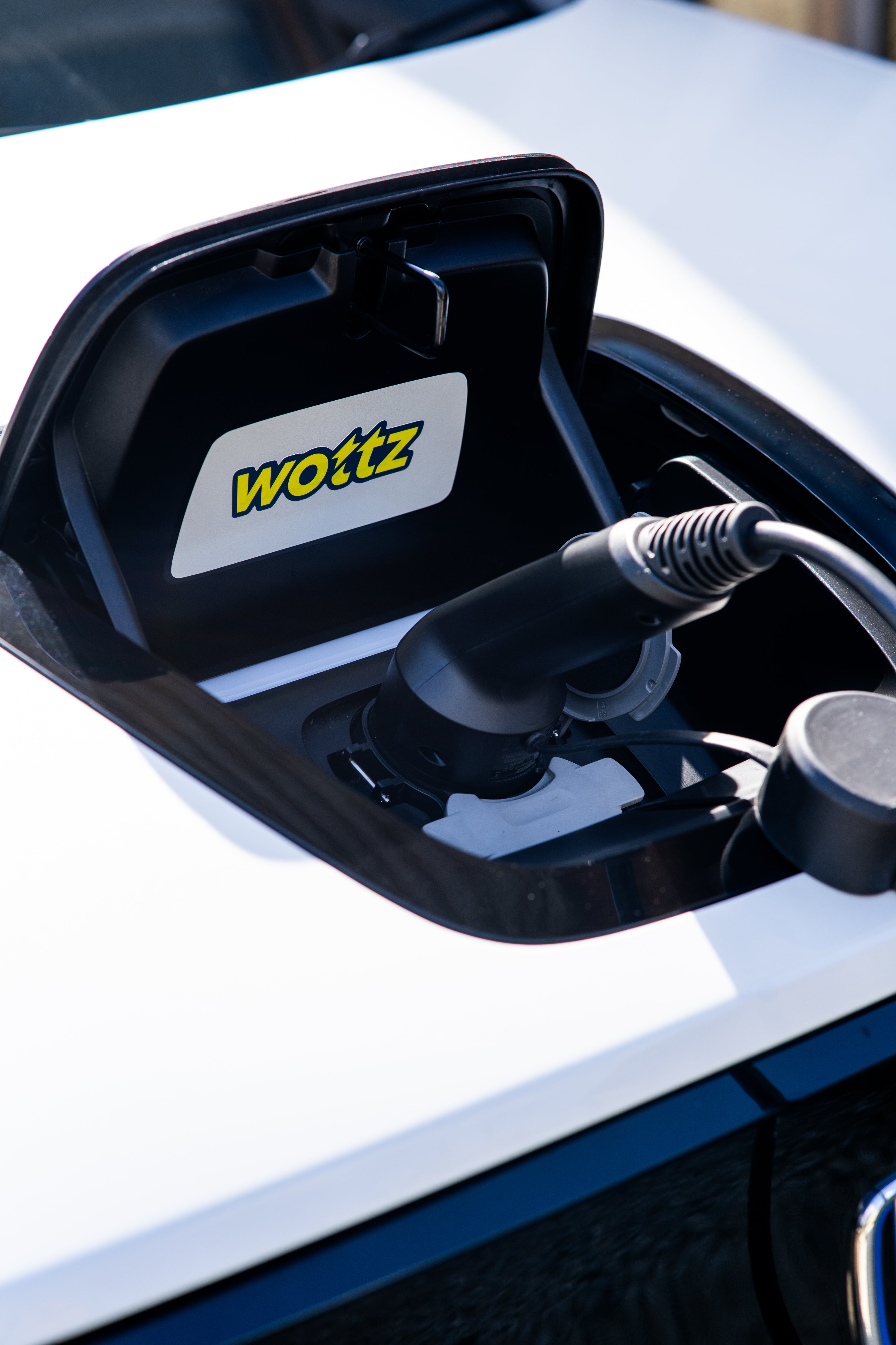 Close-up of a Wottz Type 2 plug in a white Honda e charge port with Wottz logo sticker