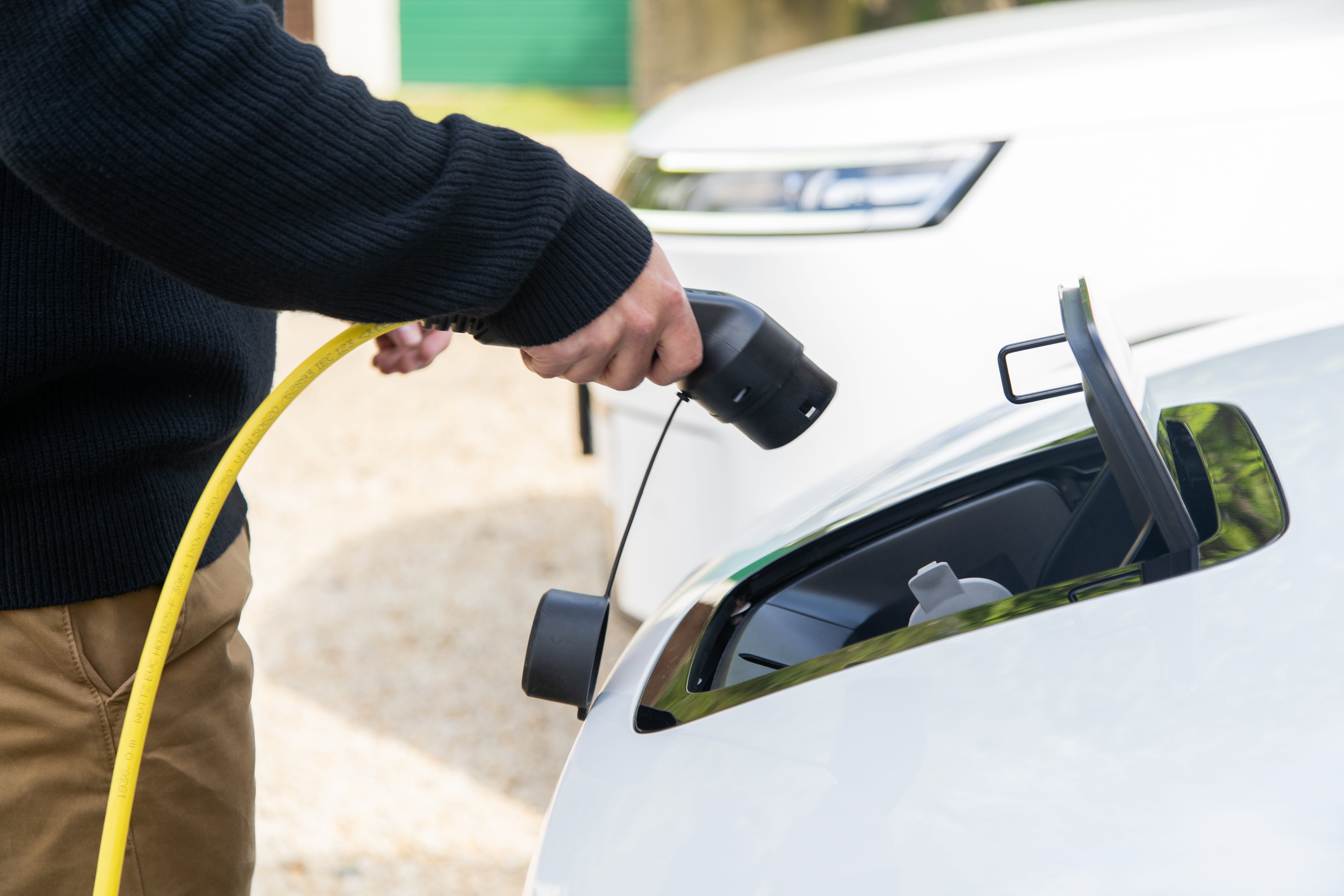 Man plugging a yellow Wottz Type 2 charging cable into a white EV charge port close-up
