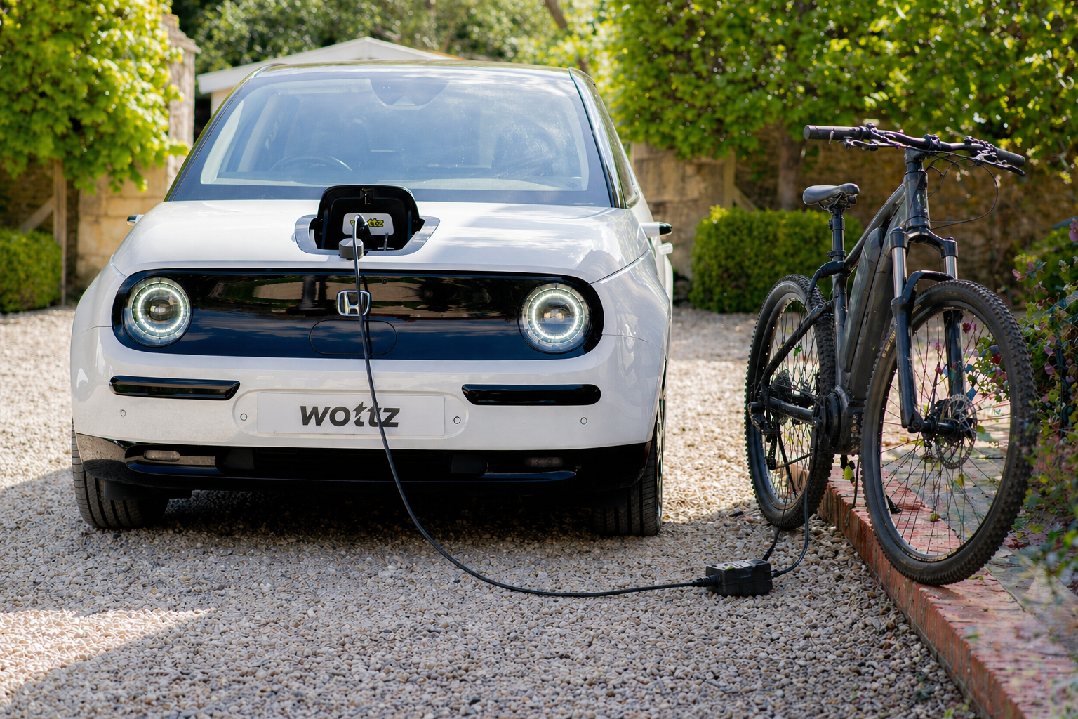 White Honda e using a Wottz V2L cable to charge an electric bicycle on a gravel driveway