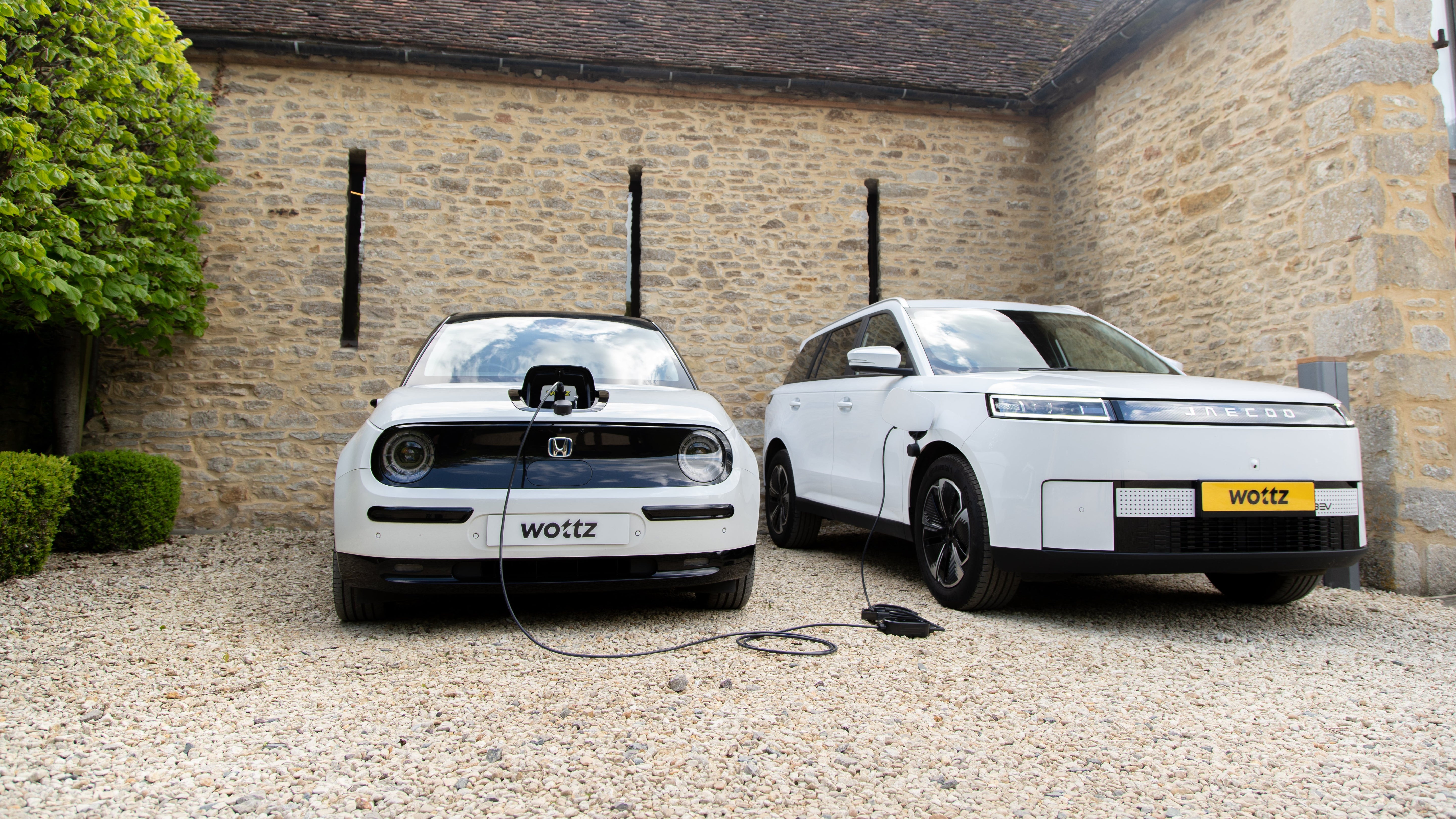 White Jaecoo SUV and Honda e connected by a Wottz V2L cable for vehicle-to-vehicle charging at a Cotswolds barn
