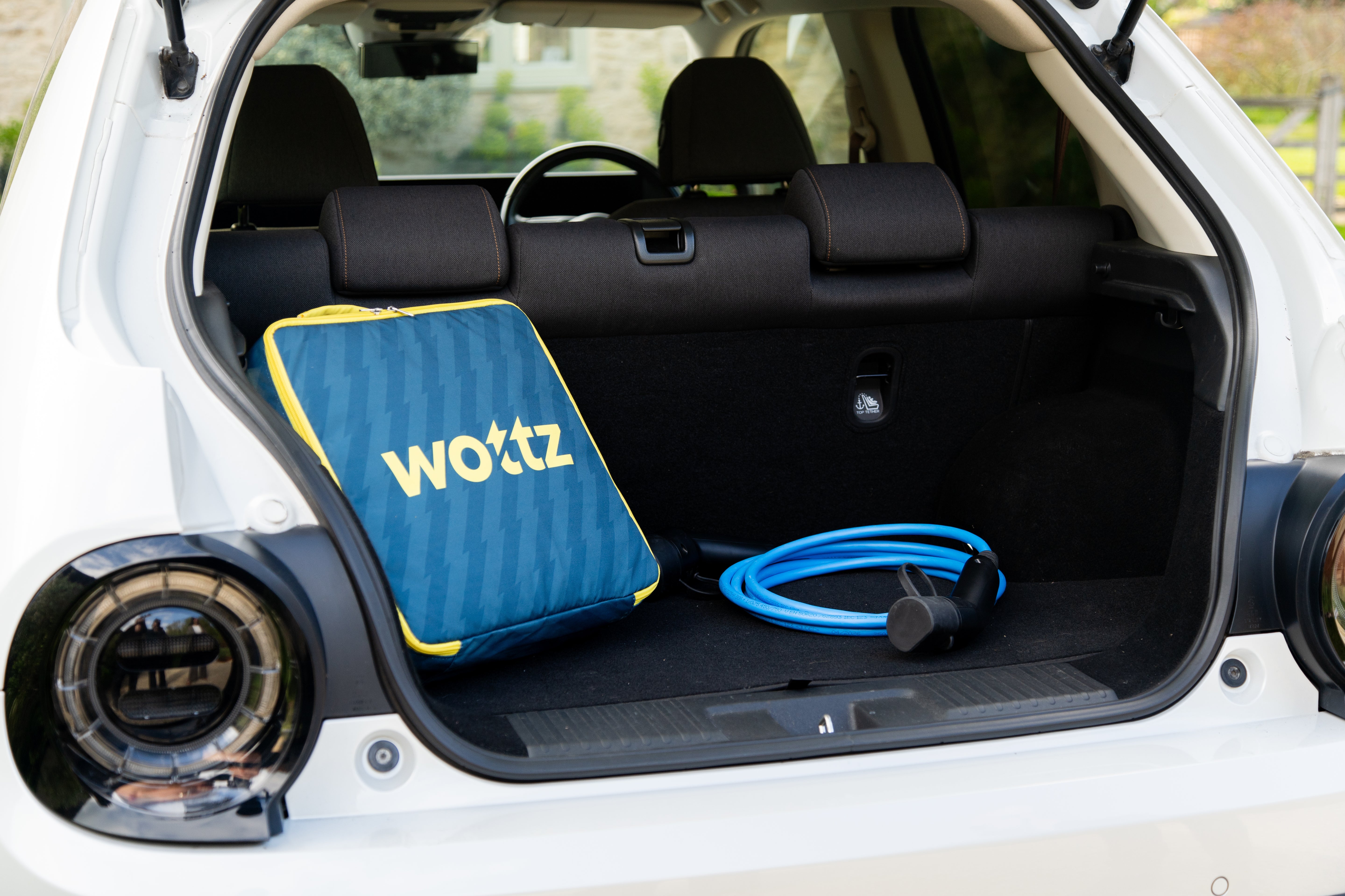 Wottz branded blue carry bag and coiled blue charging cable stored in the boot of a white Honda e