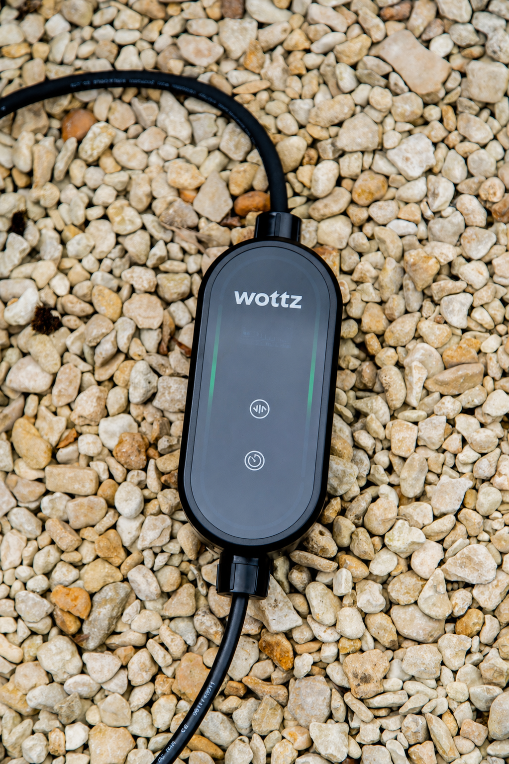 Close-up of a Wottz portable EV charger control box showing the logo and green LED indicator on gravel