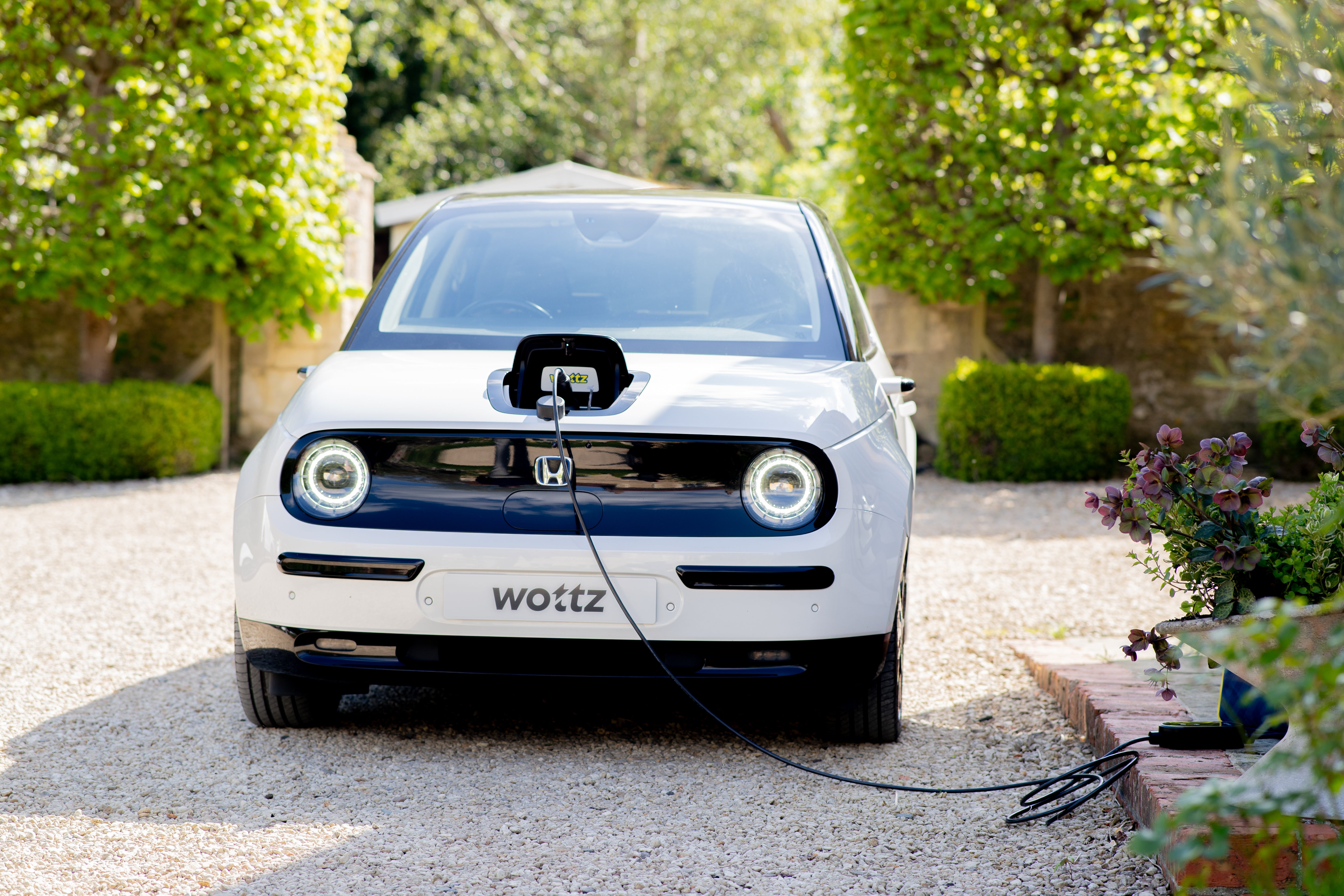 Man crouching beside a white Honda e connecting a Wottz portable charger with carry bag nearby