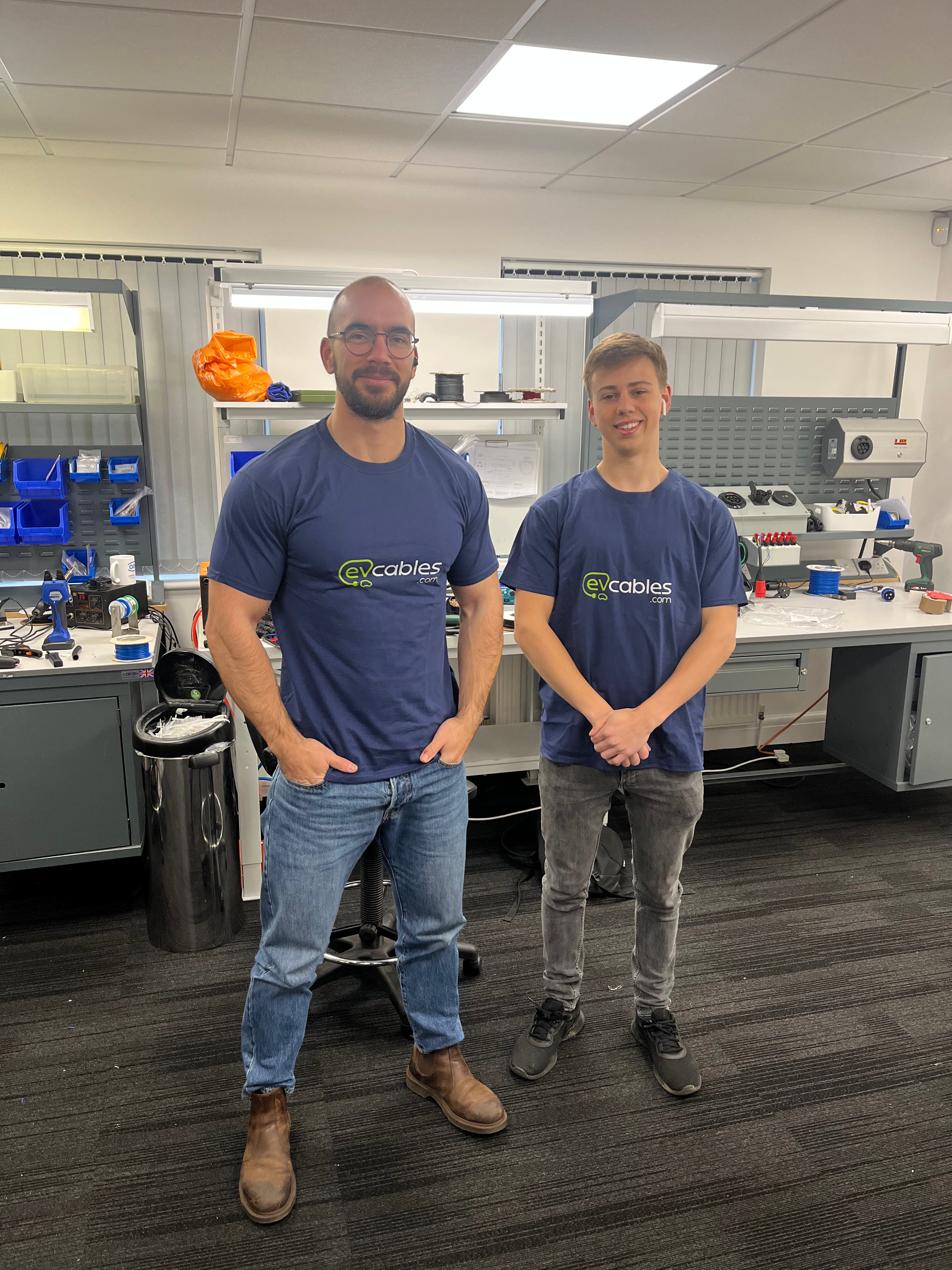 Two EV Cables team members in branded navy t-shirts standing in the company workshop surrounded by tools and cable components
