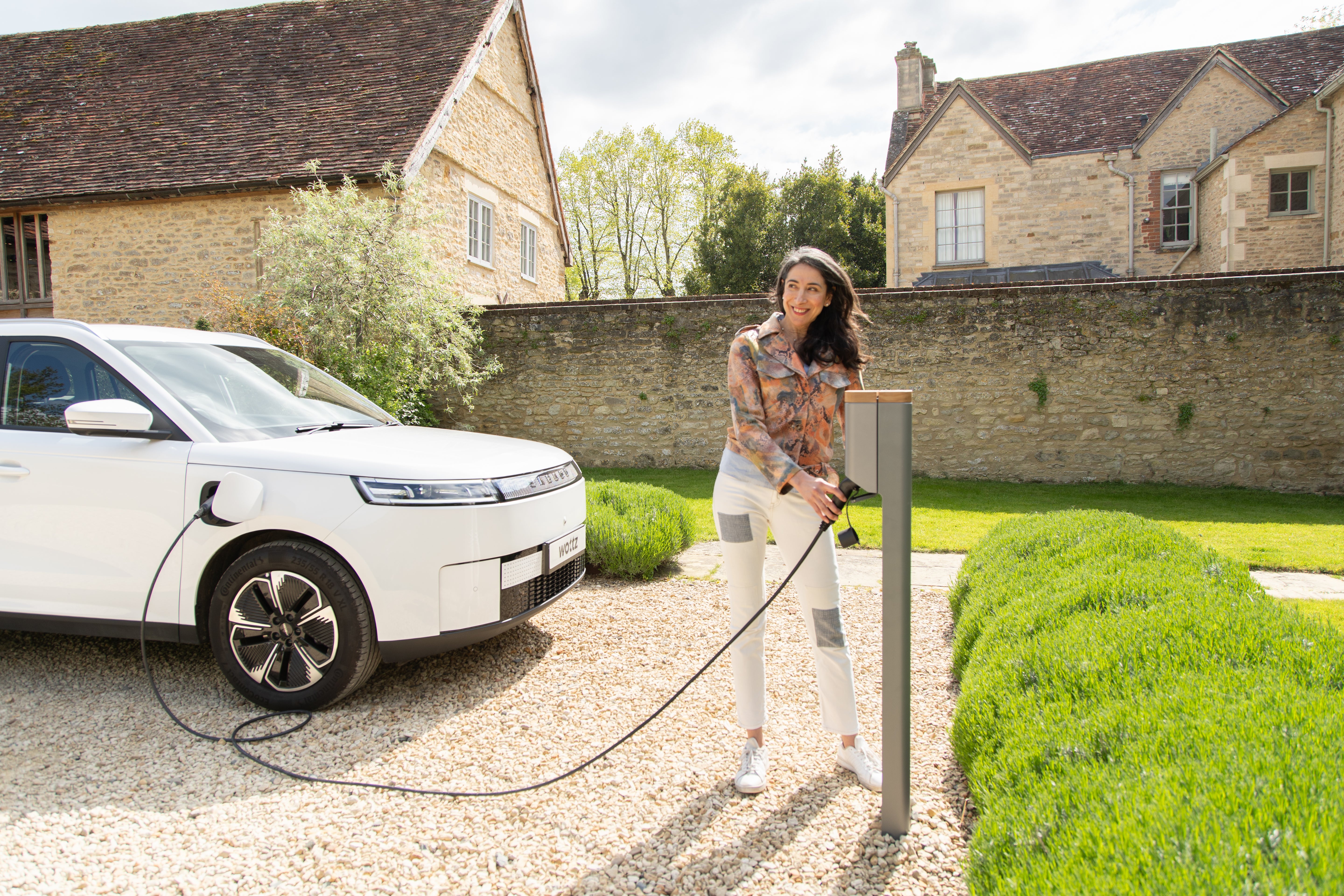Woman plugging a blue Wottz cable into a Simpson & Partners charge post with a white Jaecoo SUV in the background