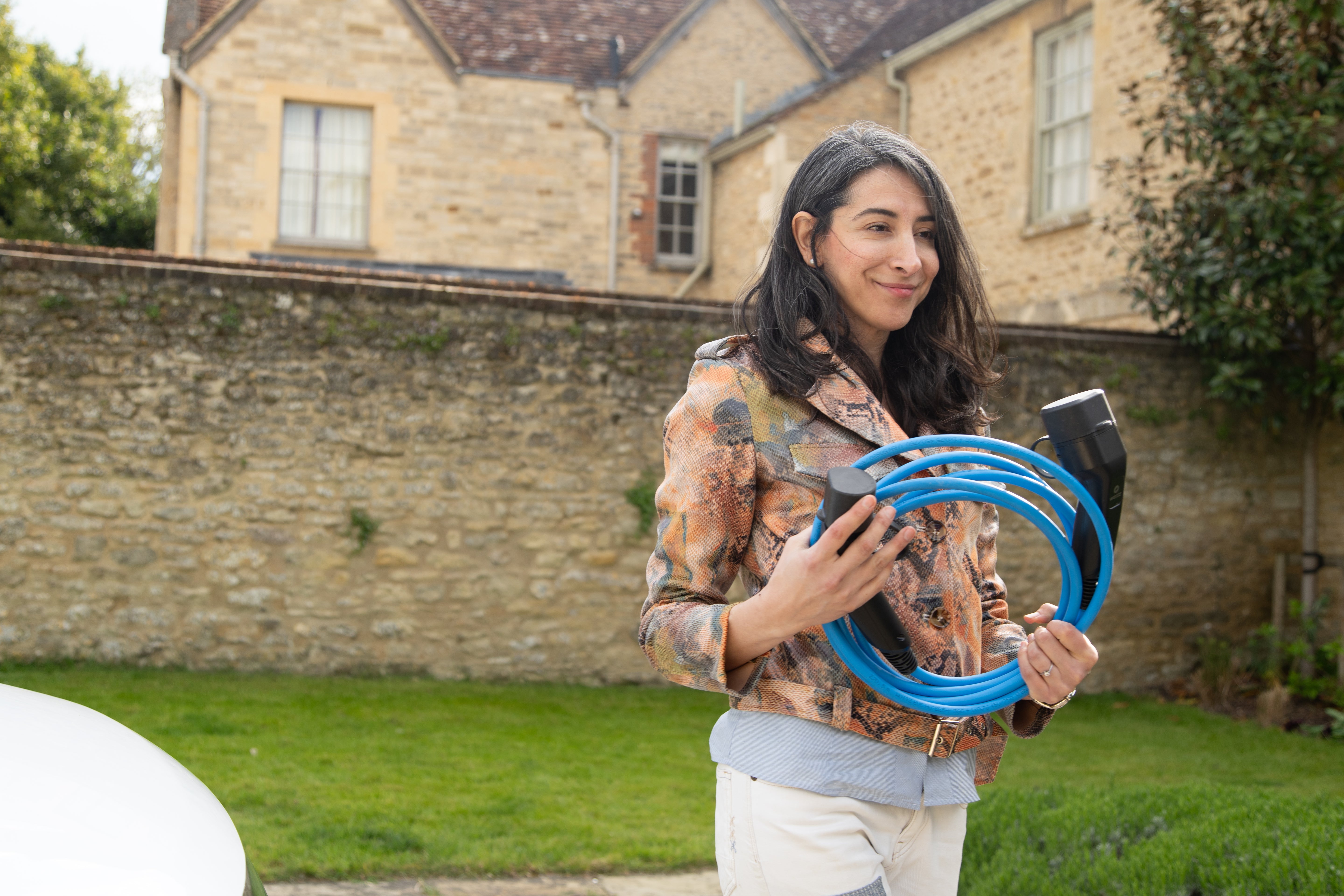 Woman holding a coiled blue Wottz Type 2 EV charging cable outside a Cotswolds stone cottage