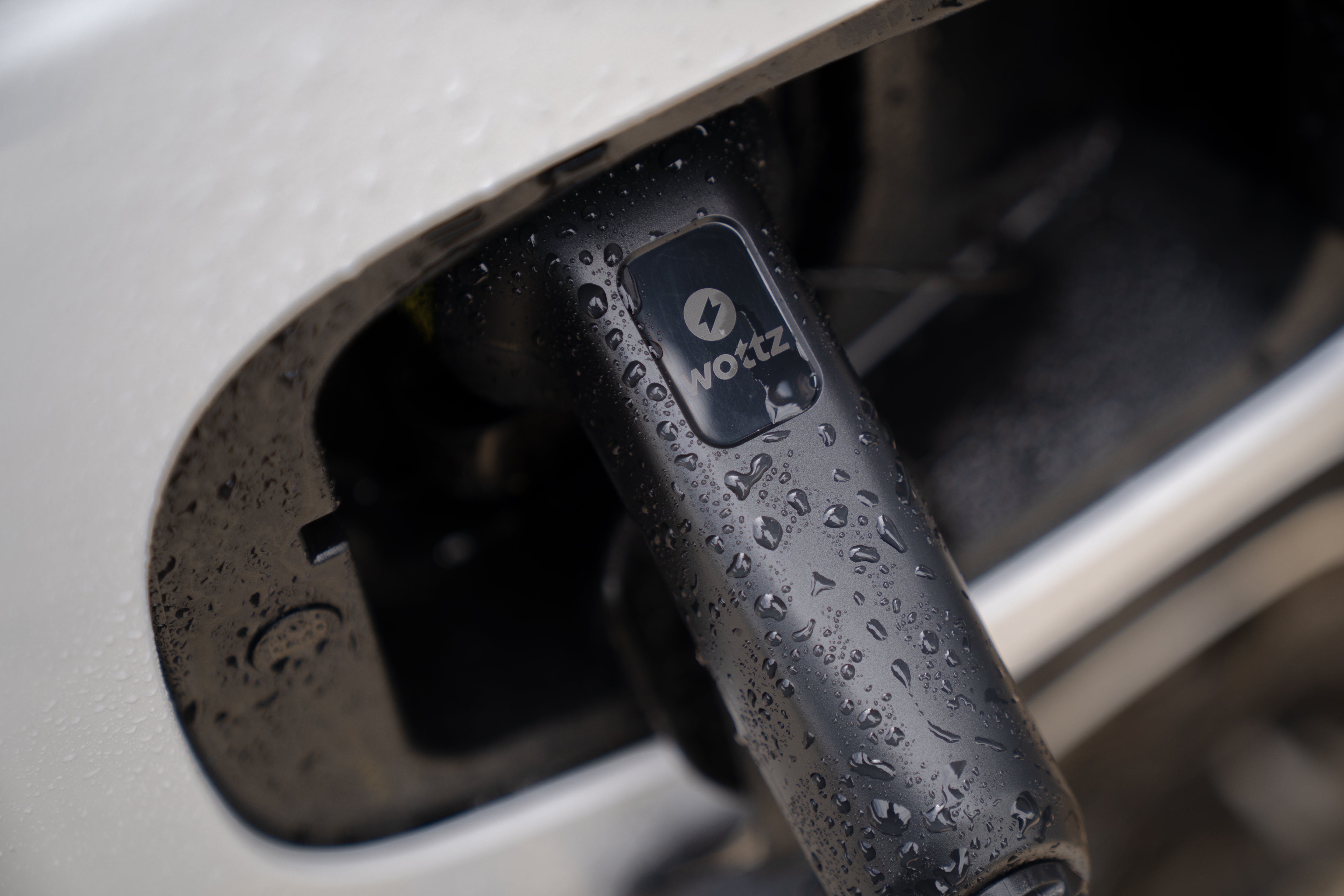 Macro close-up of a Wottz Type 2 plug handle in a charge port with rain droplets and Wottz logo
