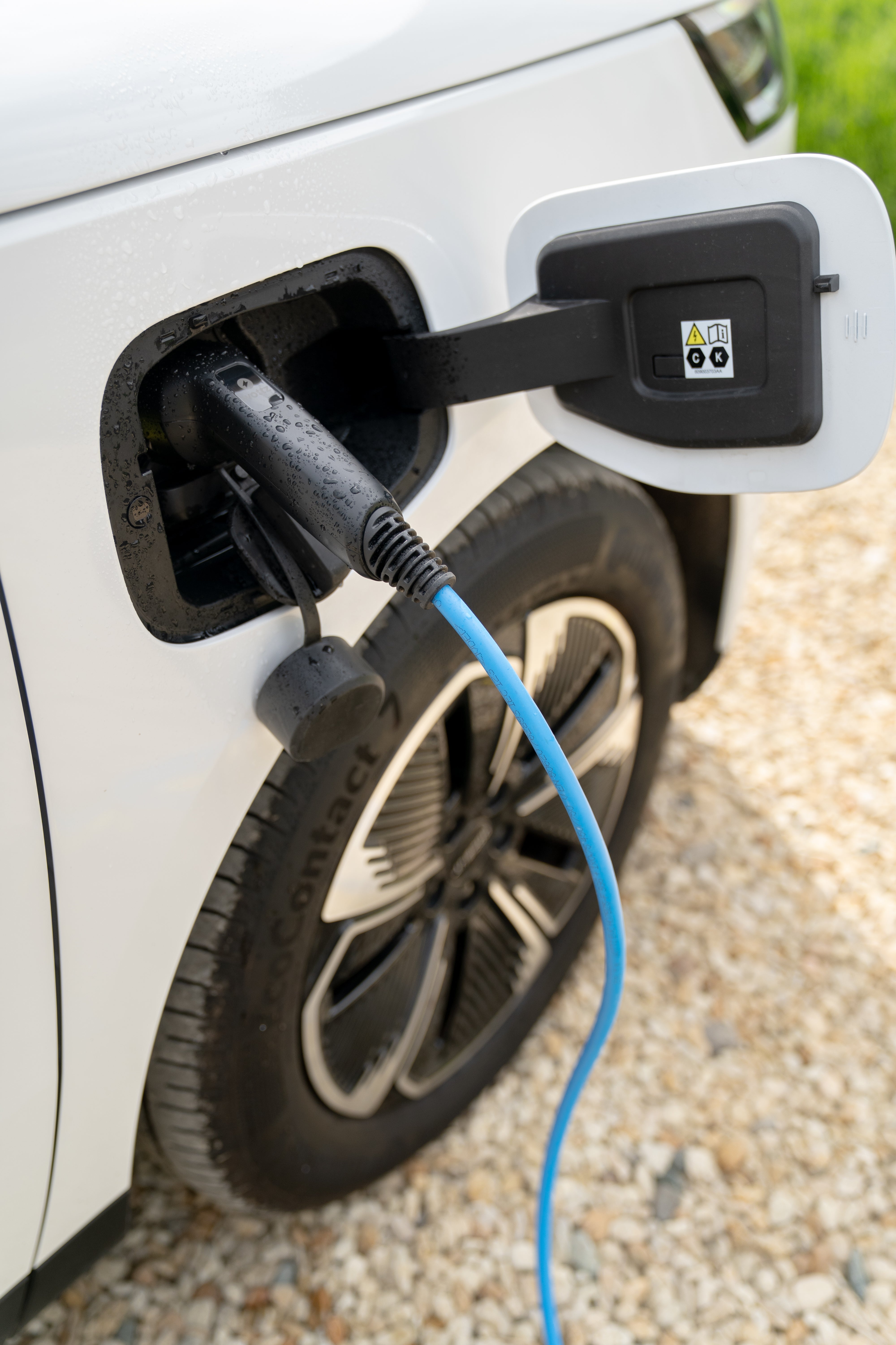 Close-up of a blue Wottz Type 2 charging cable plugged into a white Honda e charge port with rain droplets