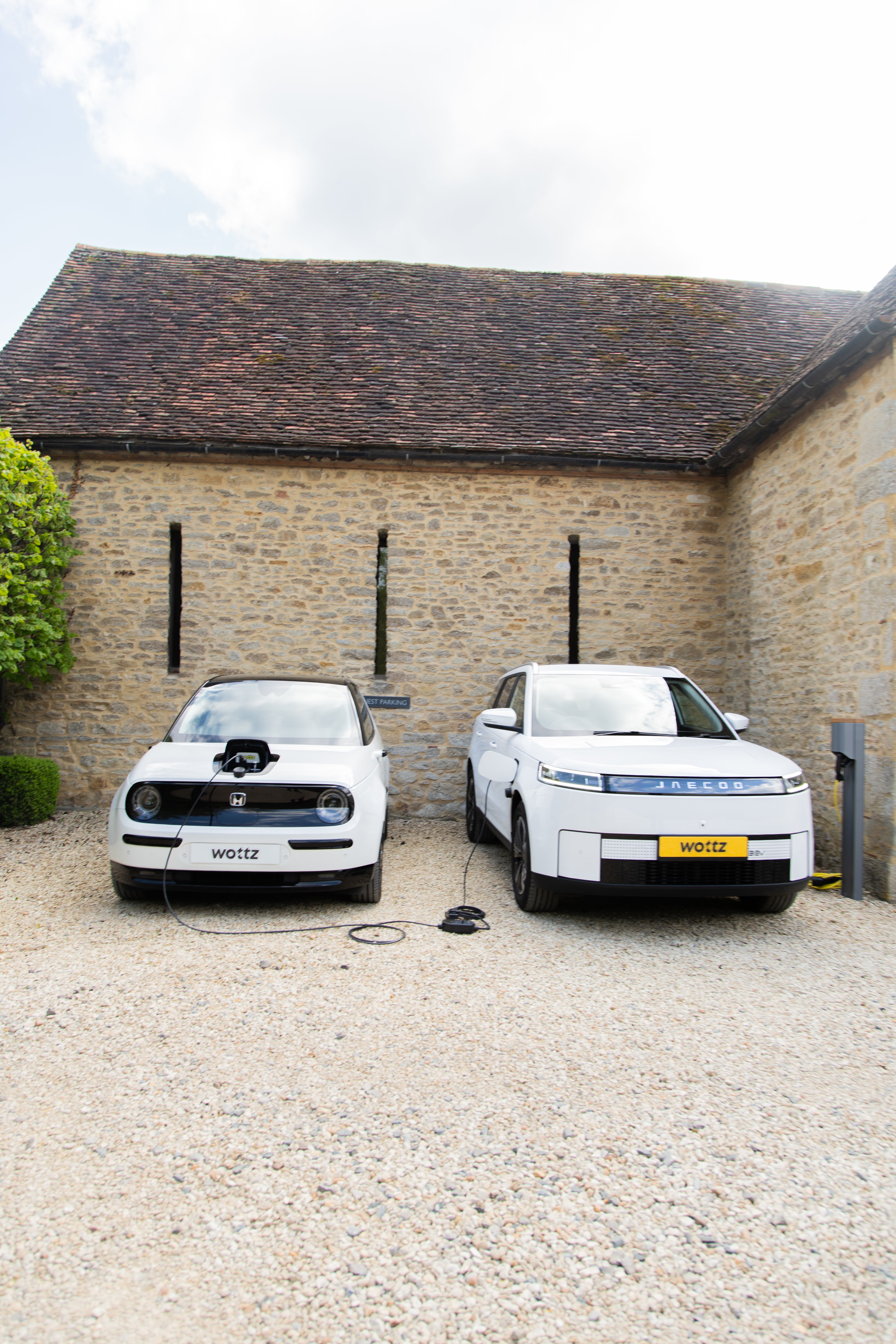 Close-up of a Type 2 connector plugged into a white Jaecoo SUV charge port at a Cotswolds stone wall